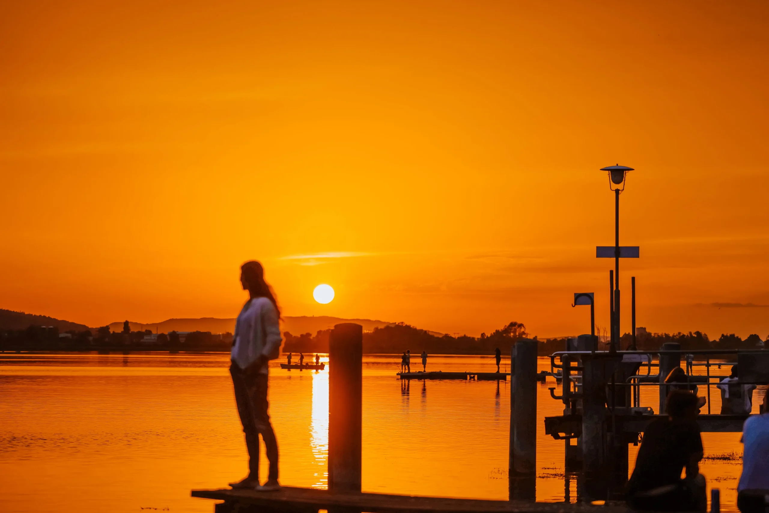 Bulimie Expertin Andrea Ammann steht in einem orange leuchtenden Sonnenuntergang auf einem Steeg an einem am See und blickt hinaus.